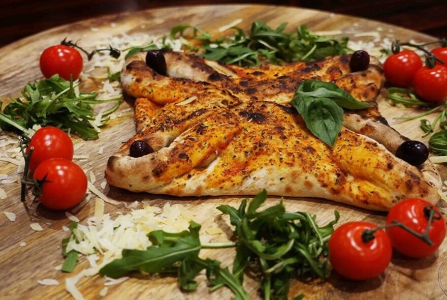 Wooden board with calzone, tomatoes, herbs and cheese.
