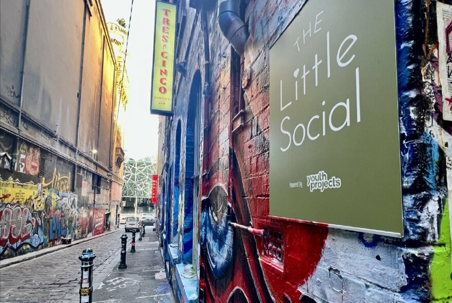 Looking south down the bluestone paved Hosier Lane, street art on the walls and a sign with the words 'The Little Social' on the wall.