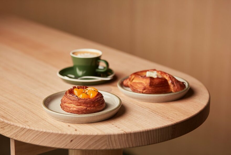 A wooden table with a coffee and two pastries. 