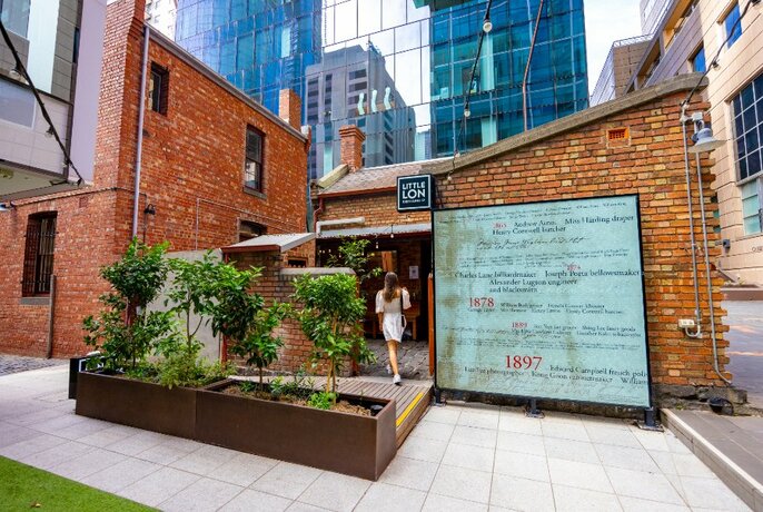 Laneway bar with historic sign, deck and plants, with city buildings in the background.