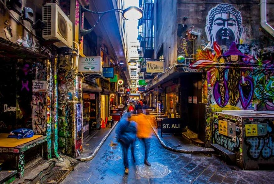 Blurred people walking through a heavily graffitied laneway. 