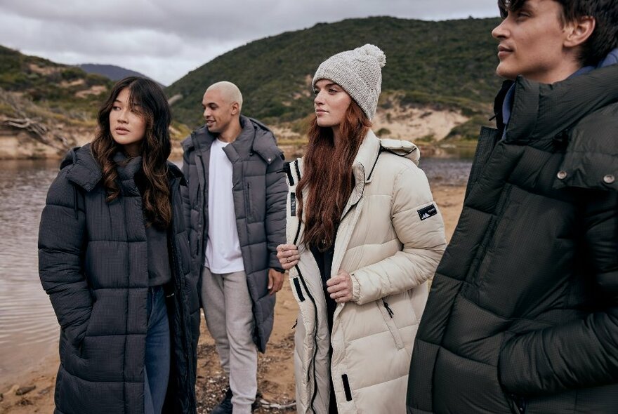 Models in a cold outdoor setting wearing long puffer jackets, and beanies.