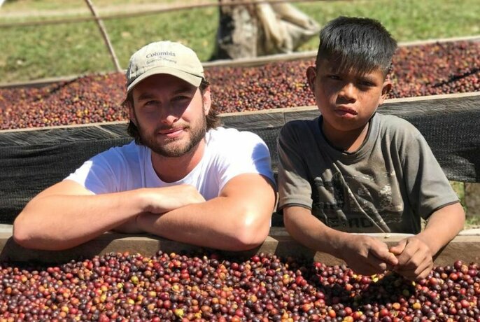 Owner and barista Billy Ballard standing with a young child behind a large container of green coffee beans.