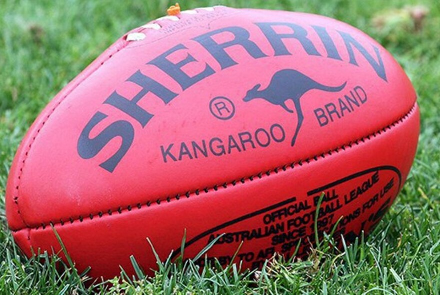 Red Sherrin brand AFL football resting on grass.