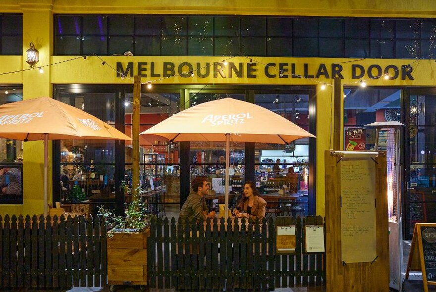 Two people sitting in front of a bar, there is a yellow umbrella