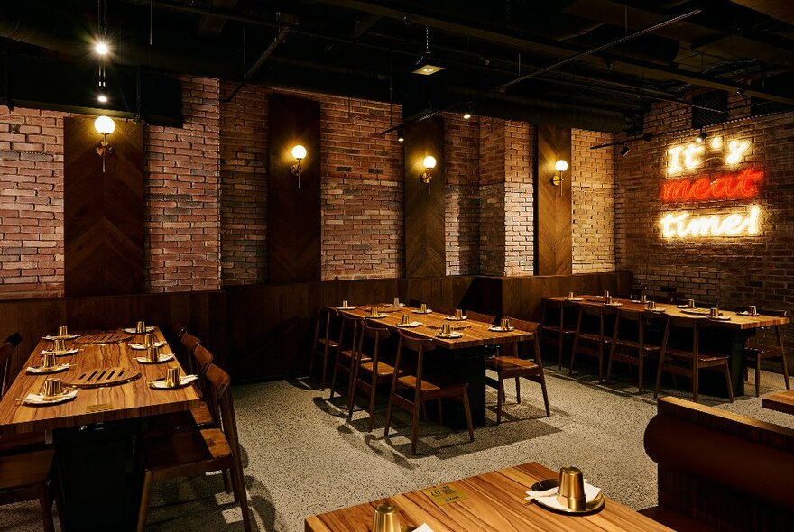 Long tables with seating and cutlery in a brick-lined, moodily lit restaurant.