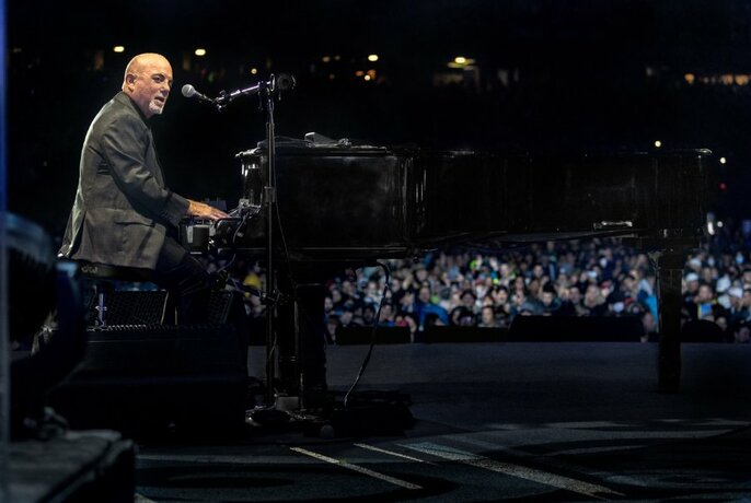 Billy Joel seated at a piano in front of an audience.