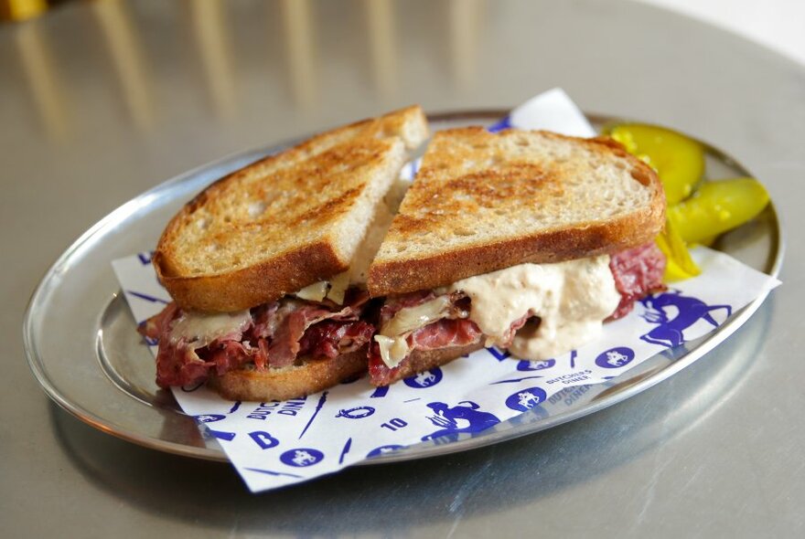 A Reuben sandwich with pickles on the side.