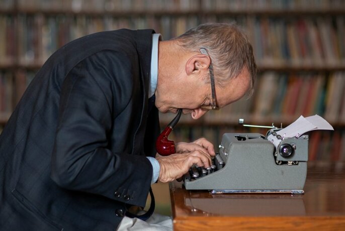 Author David Sedaris bent comically over a typewriter.
