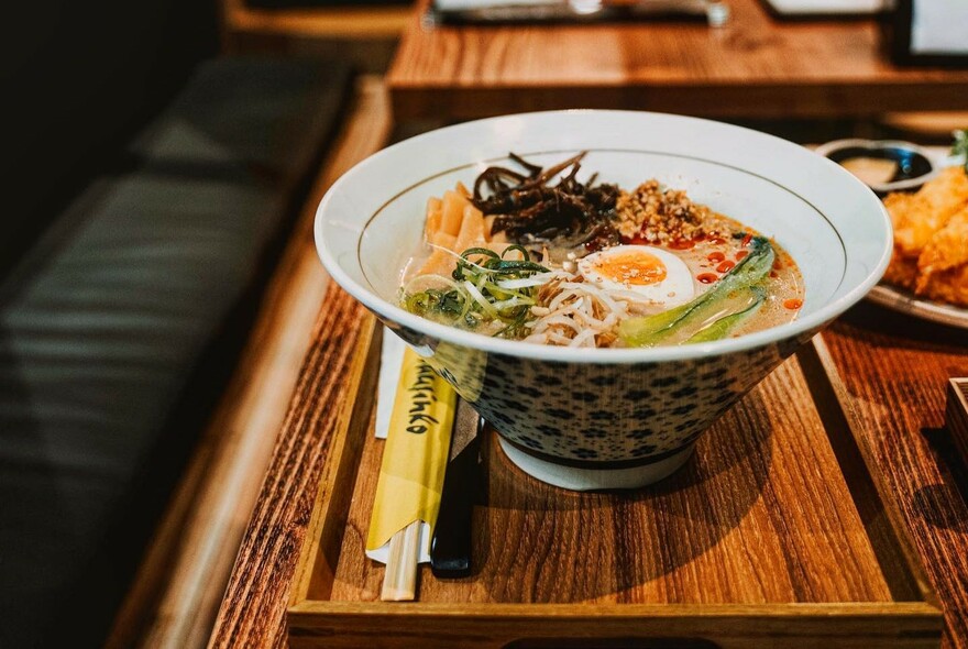 Wooden table with chopsticks and bowl of ramen with egg.
