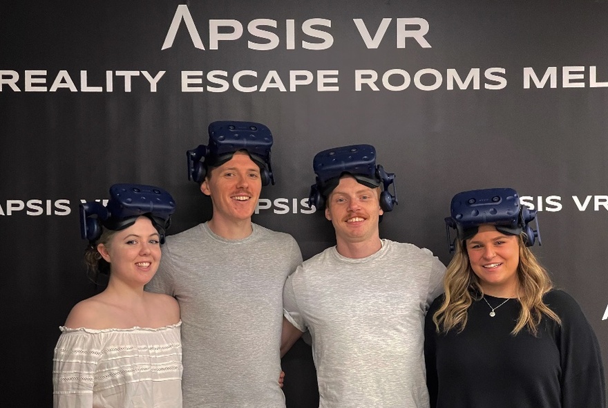 People wearing video goggles standing in front of Apsis VR logoed walls.