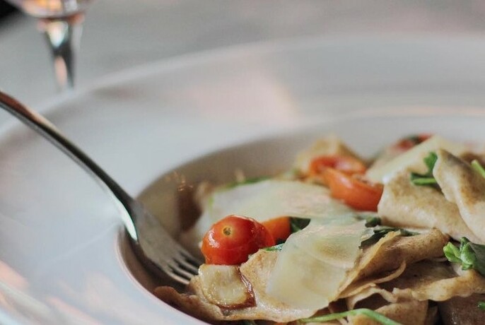 Bowl of pasta, shaved parmesan cheese and a cherry tomato.