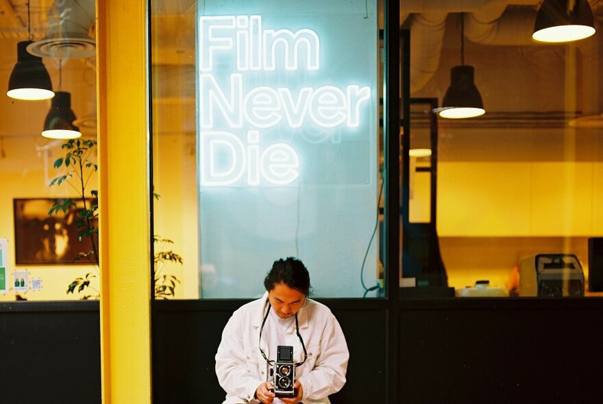Person holding an old camera in front of FilmNeverDie store.