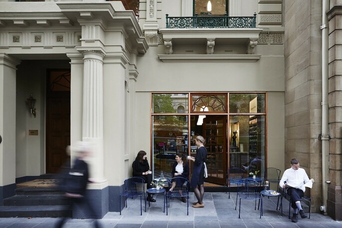 People drinking coffee at small tables outside a coffee shop on Collins Street. 