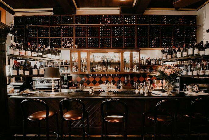 Darkly lit bar with barstools and shelves of wine bottles.