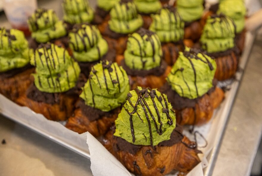 Tray of sweet croissant style pastries with green matcha topping, drizzled with chocolate.