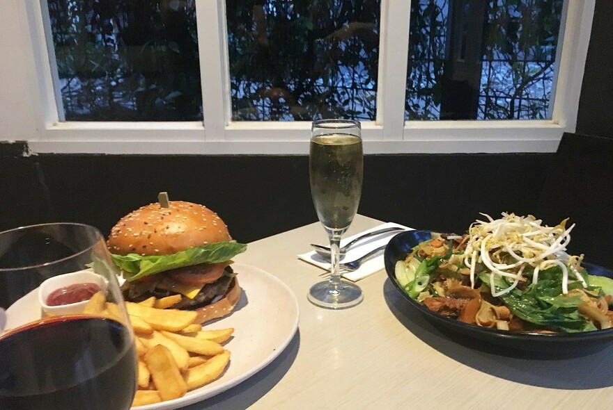 Burger and fries, glass of sparkling wine, and another meal.