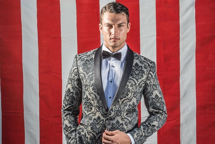 Model wearing boldly patterned tuxedo and bowtie against red striped background.