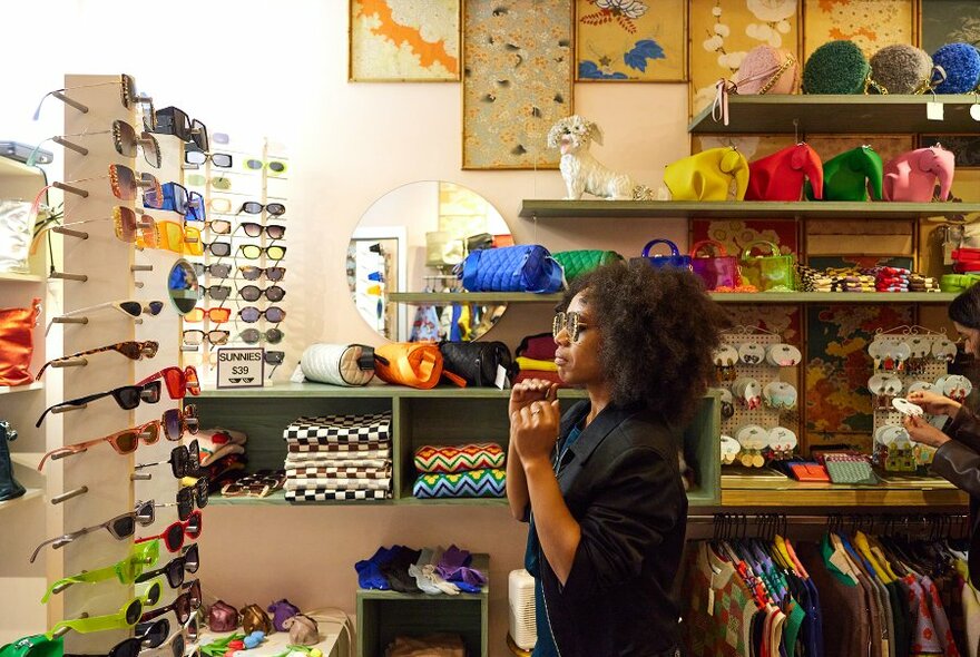 A woman trying on sunglasses in a colourful accessories boutique.