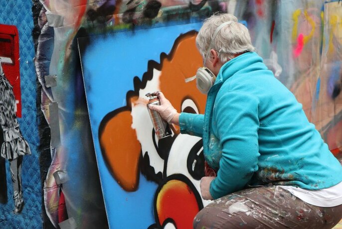 Street artist with spray can working on a midsize canvas outdoors.