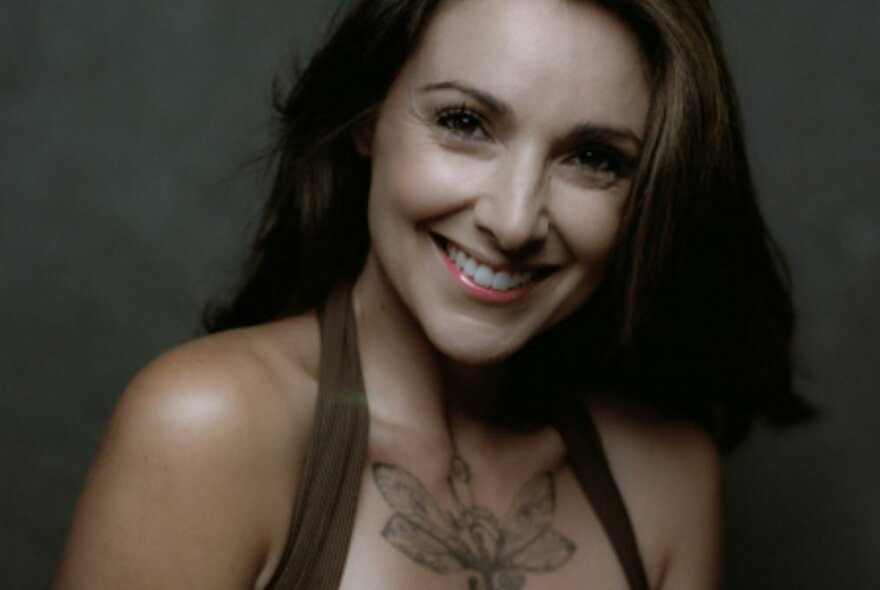 Singer Natalie Gauci smiling in a halter top with a chest tattoo showing. 