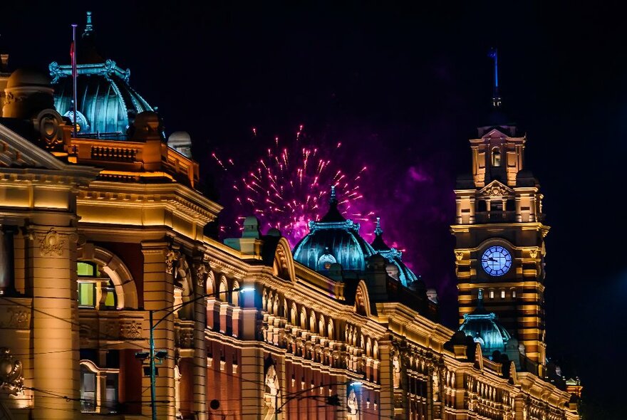 Fireworks visible over the top of illuminated Flinders Street Station at night
