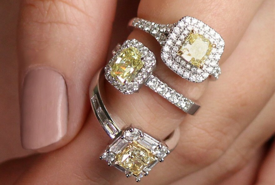 Close-up of model's hand with three yellow diamond rings on one finger.