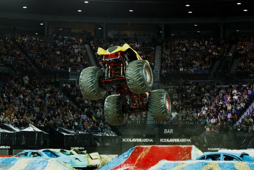 A monster truck with oversize tyres in a mid-air jump inside a crowd-filled stadium arena.