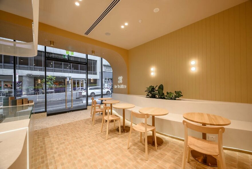 Sleek and modern interior of a cake shop with small tables and chairs facing a banquette wall. against the wall.