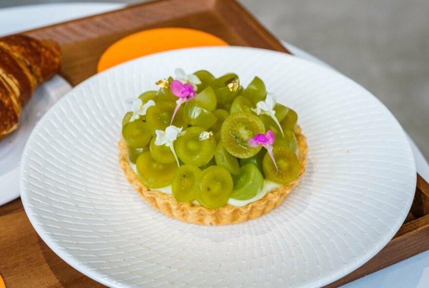 A tart topped with green grapes and edible flowers.
