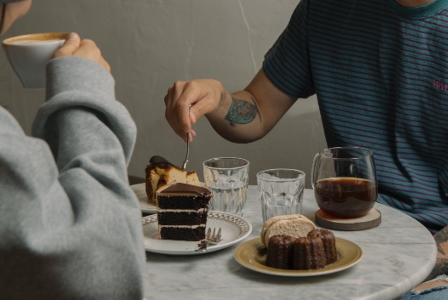 A small table with two people enjoying coffee and cakes.