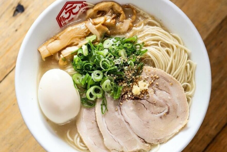 A bowl of ramen with meat, spring onions and egg.