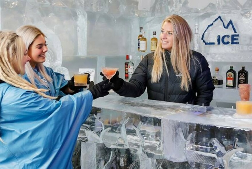 Bartender handing drinks to two customers over a bar constructed from ice. 