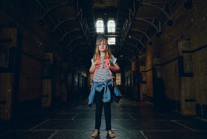 A young girl standing in a dark corridor in Old Melbourne Gaol.