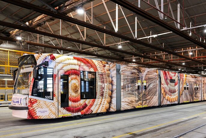 A tram painted with artworks, parked in an undercover tram terminus.