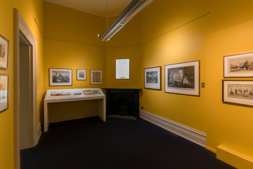 Displays and artworks hanging on the yellow-painted walls of an exhibition room.