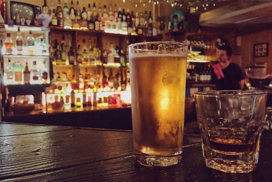View of a bar with a glass of beer and a whiskey in the foreground. 