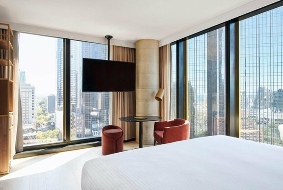 Luxury hotel room with white linen double bed facing floor to ceiling windows, sparse modern decor.