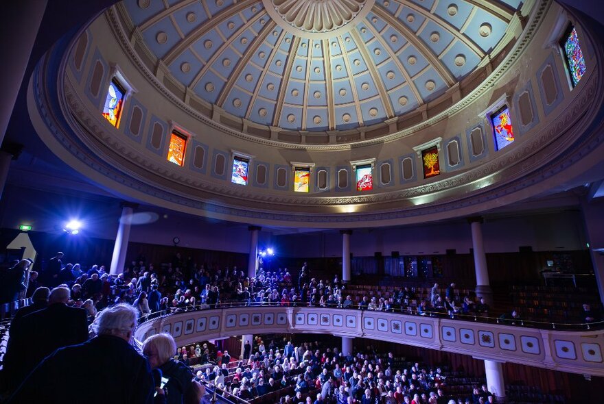 View from a mezzanine seating area in a venue, looking over the audience seated in stalls and up to a large Pantheon-like dome.