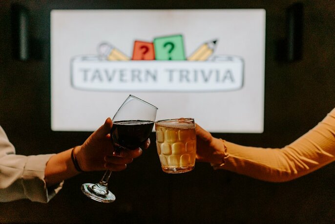 Wine glass and beer glass being 'cheersed' with Tavern Trivia banner in background.