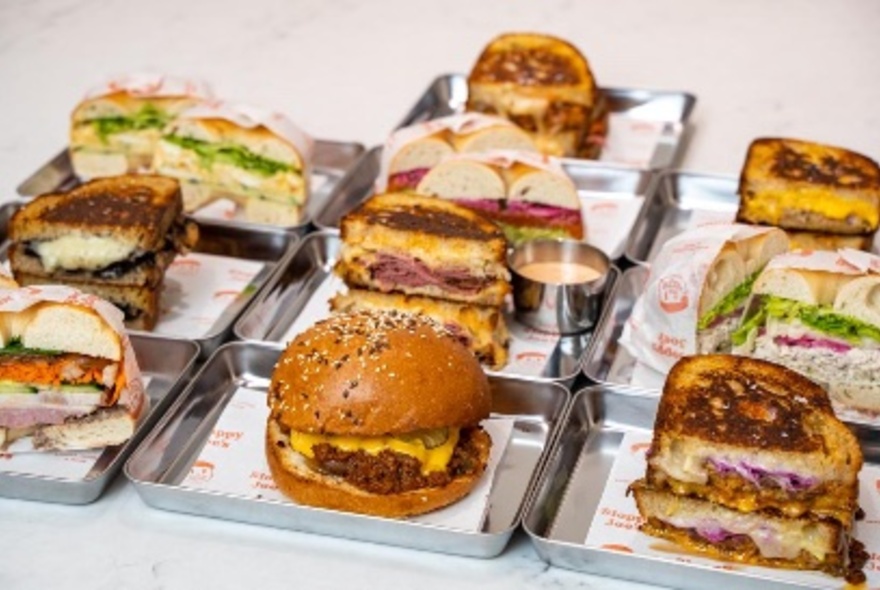 Metal trays lined up with burgers on serviettes.