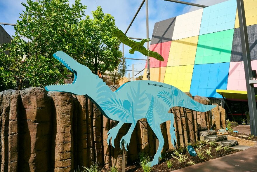 A blue cut out of a dinosaur in a garden outside the colourful Melbourne Museum building.