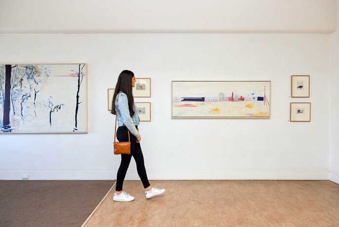 Person walking past artworks on a gallery wall.