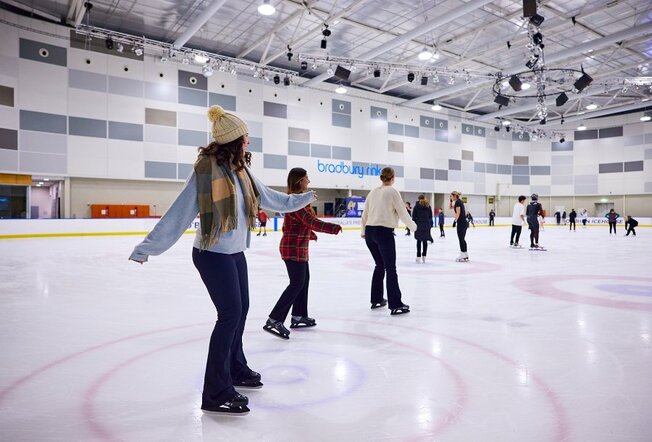 Crowds of people ice skating on an indoor rink.