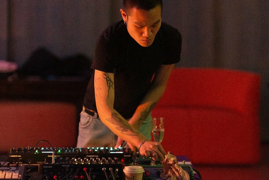 A DJ twiddling knobs on a music desk with drinks.