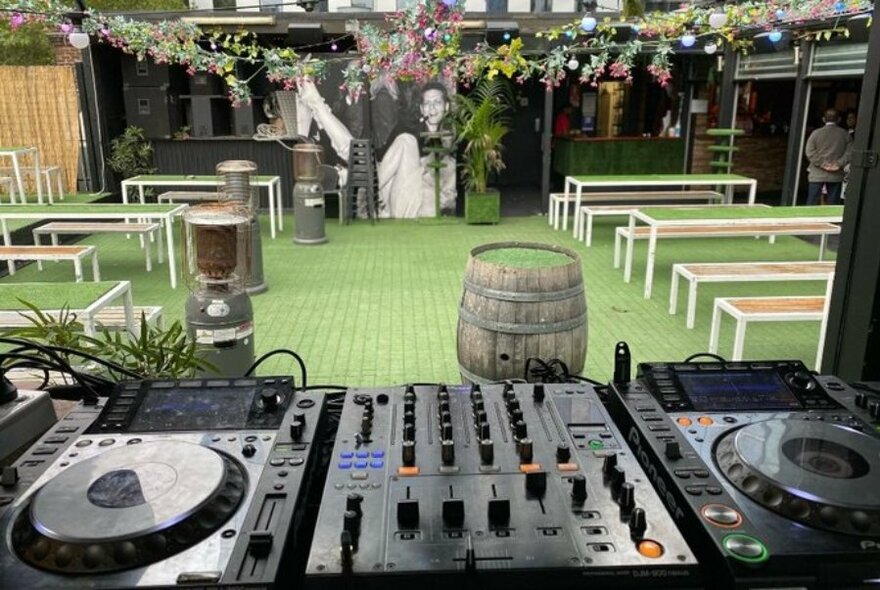 A grassy rooftop bar with a mural, flowers, and a DJ deck