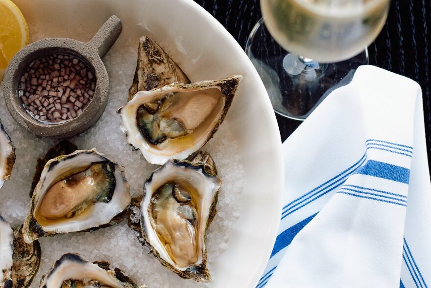 A plate with oysters on a bed of salt, a white and blue cloth and a glass of champagne. 
