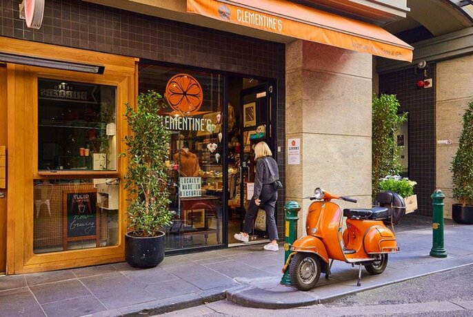 Person walking into shop with orange Vespa scooter outside.