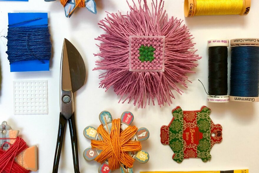 overhead view of craft items used in making a fabric brooch including sewing thread, scissors, and coloured yarn on spools.
