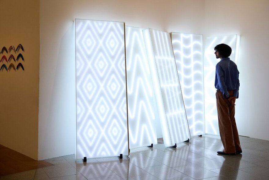 A man looking at a glowing art installation with panels of patterned lights.